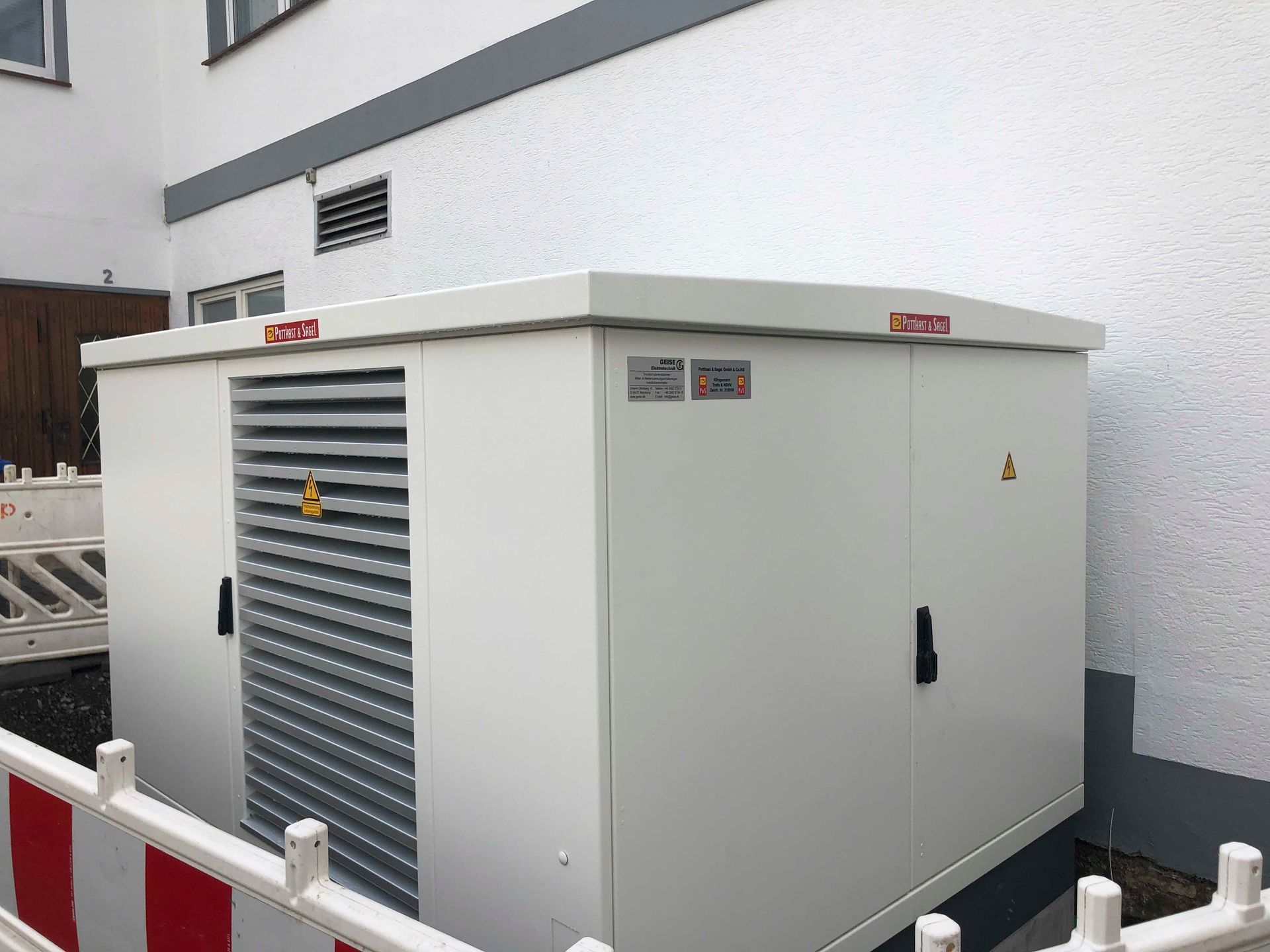 Weißer elektrischer Transformatorkasten mit Belüftung vor einer weißen Gebäudewand