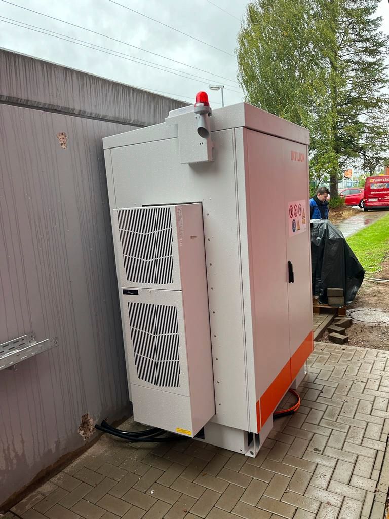 Großer, weiß-roter elektrischer Generator vor einer Betonwand, mit einem blinkenden roten Licht darauf.