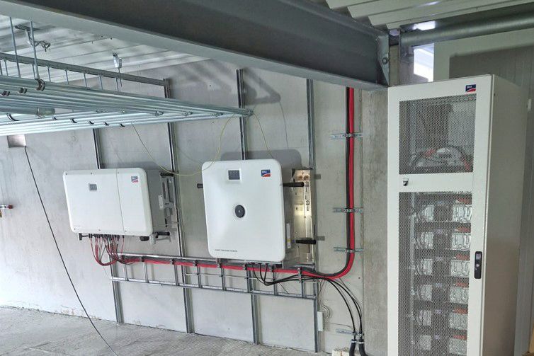 Solarwechselrichter und Batterieschrank sind an einer Betonwand montiert. Die elektrische Verkabelung ist sichtbar.