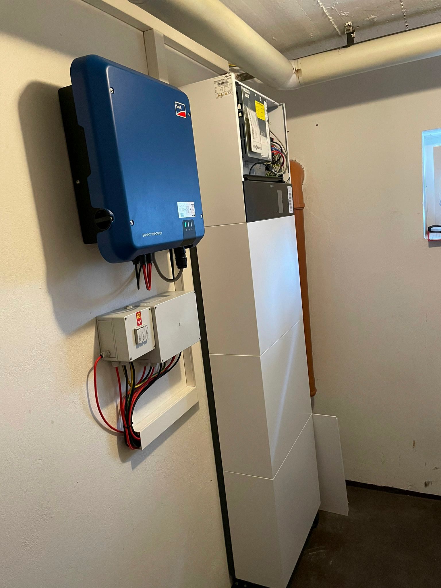 Ein blauer Solarwechselrichter und weiße elektrische Bauteile sind an einer Wand montiert.