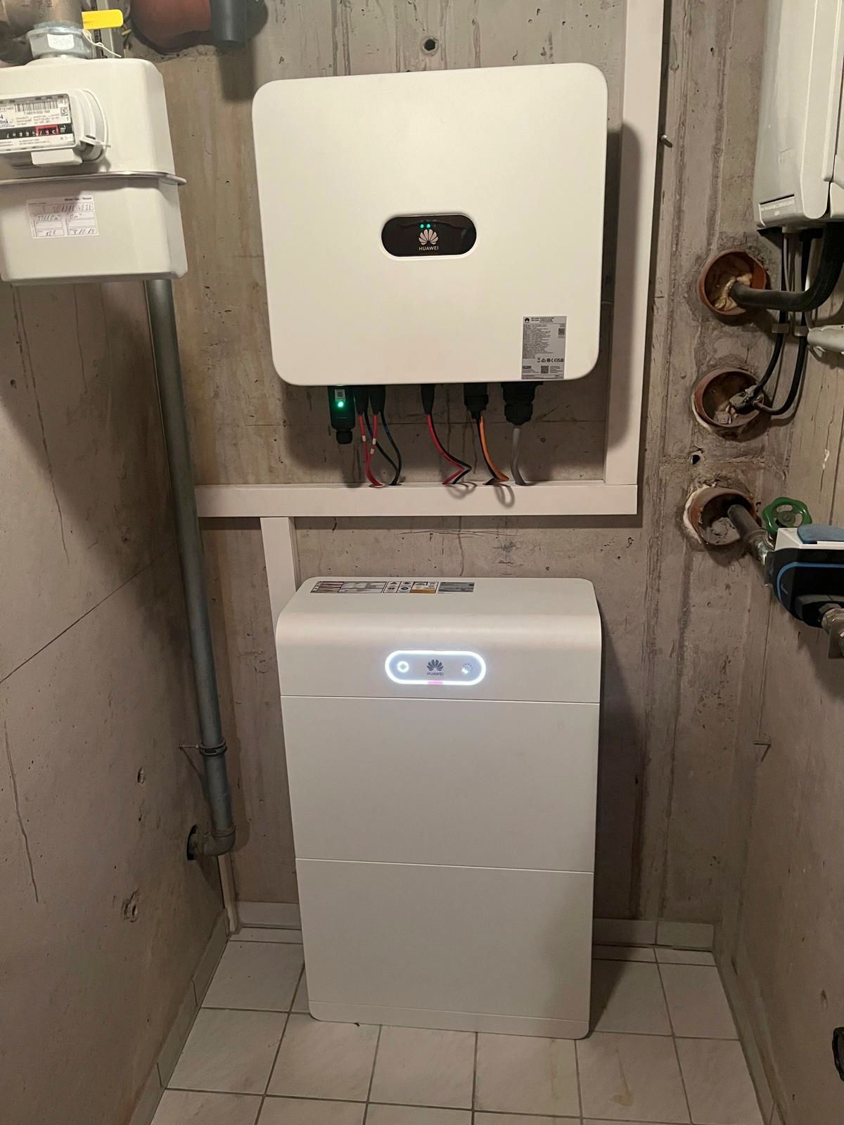 Weißer Solarwechselrichter und Batterie, installiert in einem Hauswirtschaftsraum an einer Betonwand.