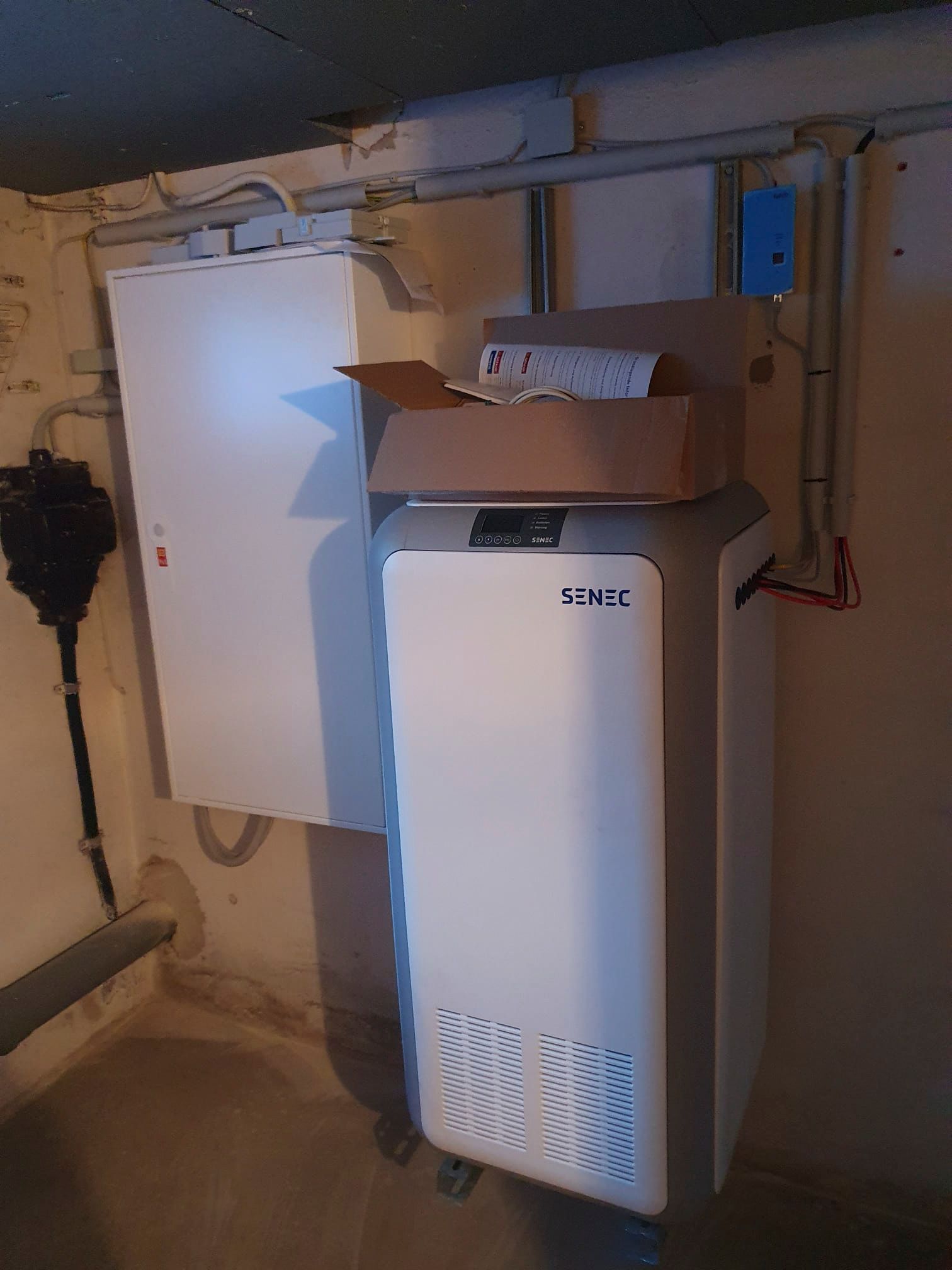 Weißer Schaltschrank und Heizgerät im Keller, Rohre und Leitungen sichtbar.