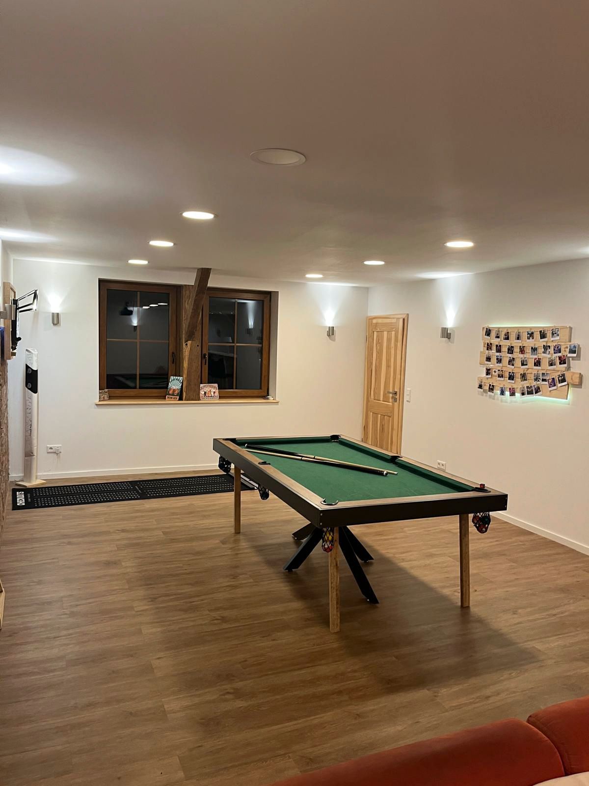 Billardtisch in einem ausgebauten Keller mit Holzbodenoptik und Einbaustrahlern. Im Hintergrund ist ein Fenster zu sehen.