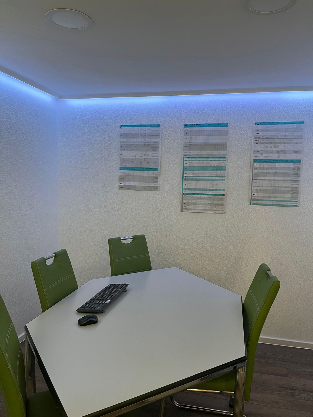 Besprechungsraum mit weißem Tisch, grünen Stühlen und Postern an der Wand.