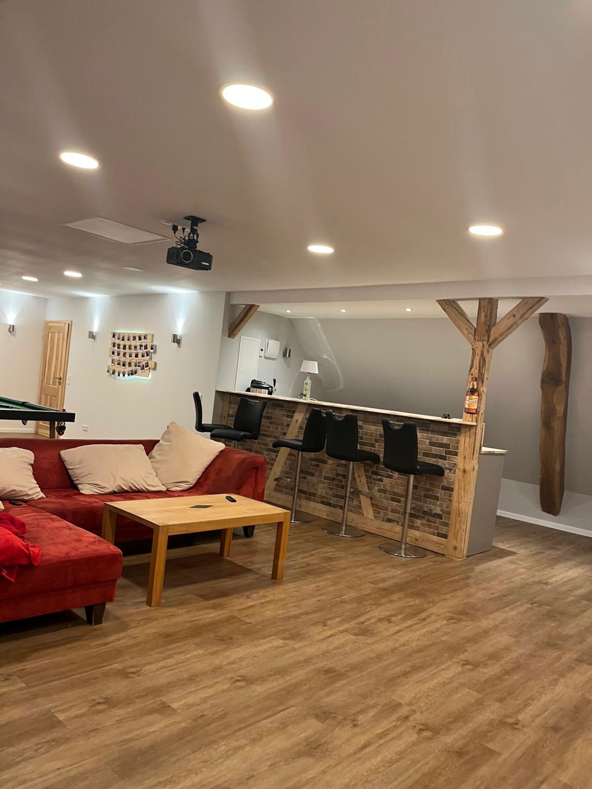 Unterhaltungsbereich im Untergeschoss mit roter Eckcouch, Holzbar, Projektor und Einbauleuchten.