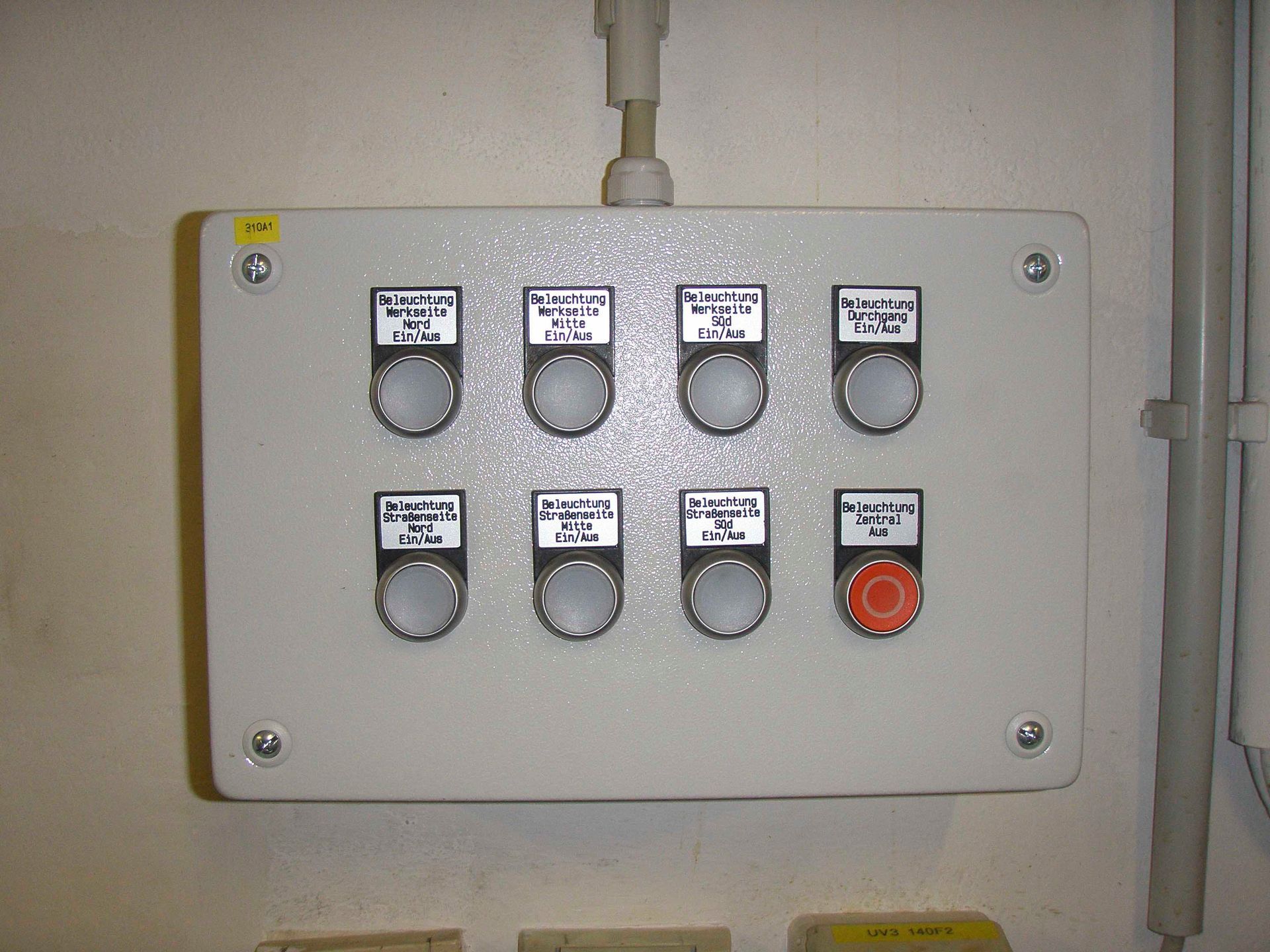 Bedienfeld mit acht beschrifteten Tasten und einem roten Not-Aus-Knopf.