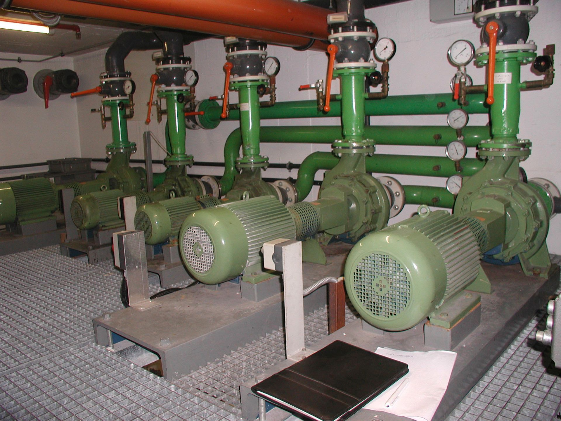 Vier grüne Industriepumpen mit Rohren und Manometern in einem Technikraum.