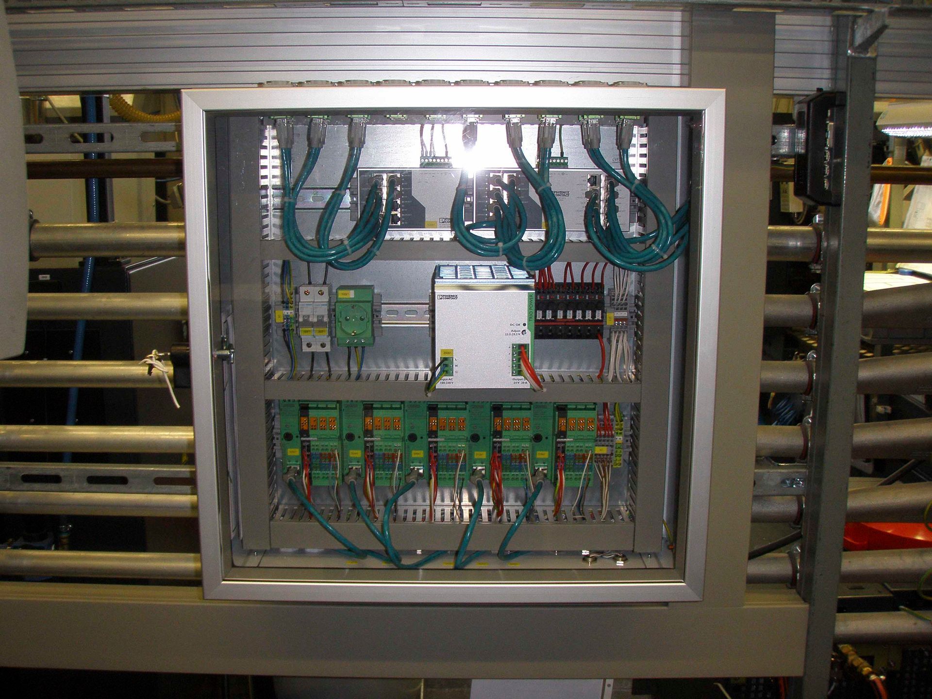 Bedienfeld mit grünen Kabeln, Digitalanzeigen und elektrischen Bauteilen in einem Metallgehäuse.