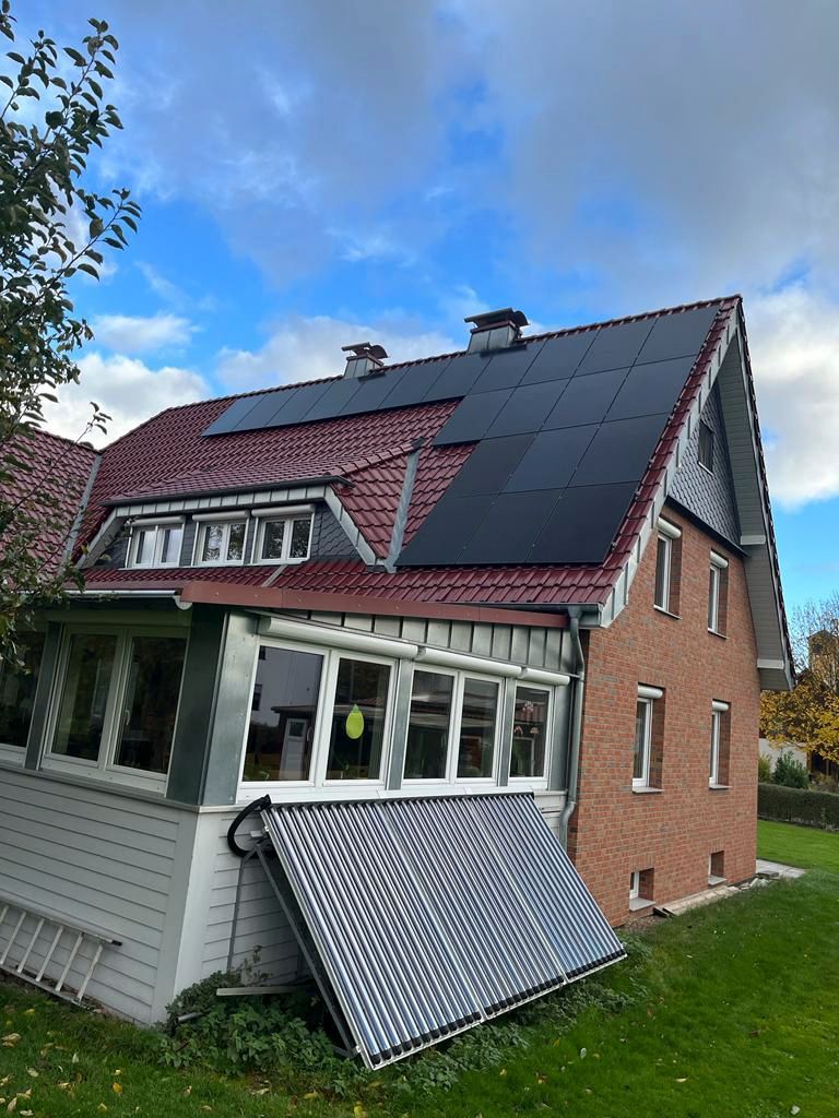 Auf dem roten Ziegeldach eines Hauses mit Backsteinfassade und weißer Veranda wurden Solarpaneele installiert.