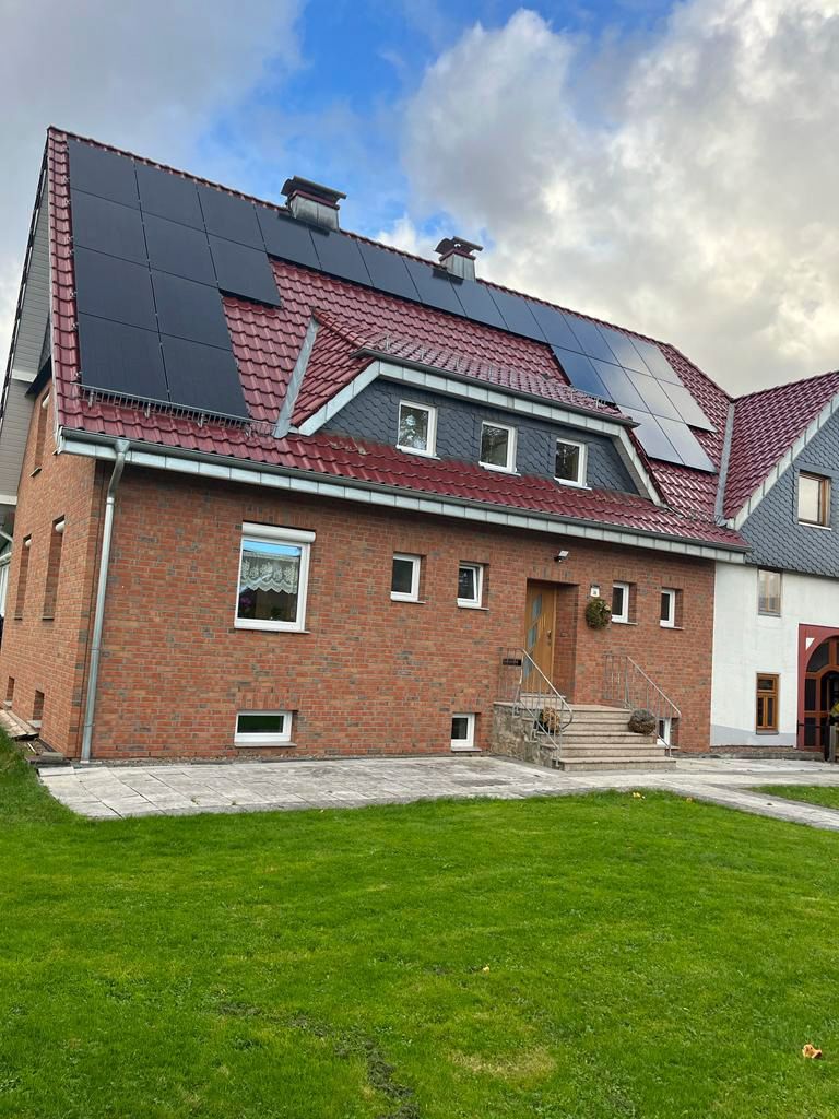 Backsteinhaus mit rotem Dach, Solaranlage und grünem Rasen. Bewölkter Himmel im Hintergrund.