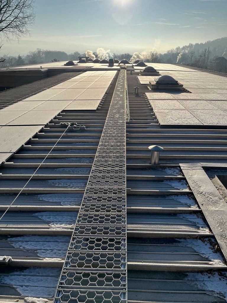 Metallsteg auf einem schneebedeckten Dach. Sonniger Tag mit Bäumen in der Ferne und Nebel.