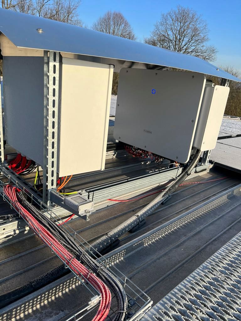 Zwei beigefarbene Elektroverteilerkästen mit Metalldach auf einem Dach, an denen viele Kabel hängen.