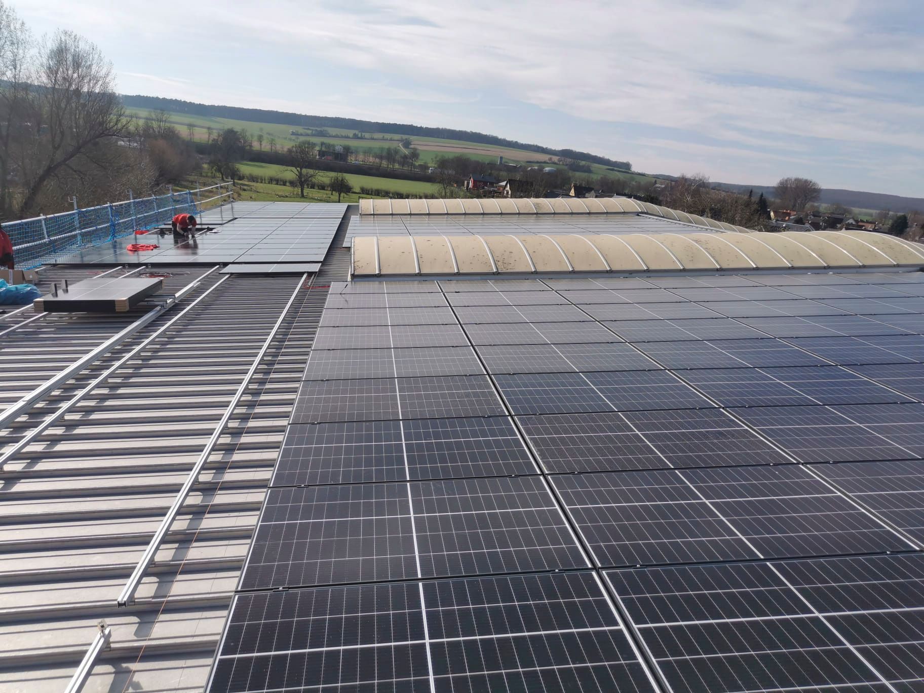 Auf einem Dach vor bewölktem Himmel werden Solarpaneele installiert.