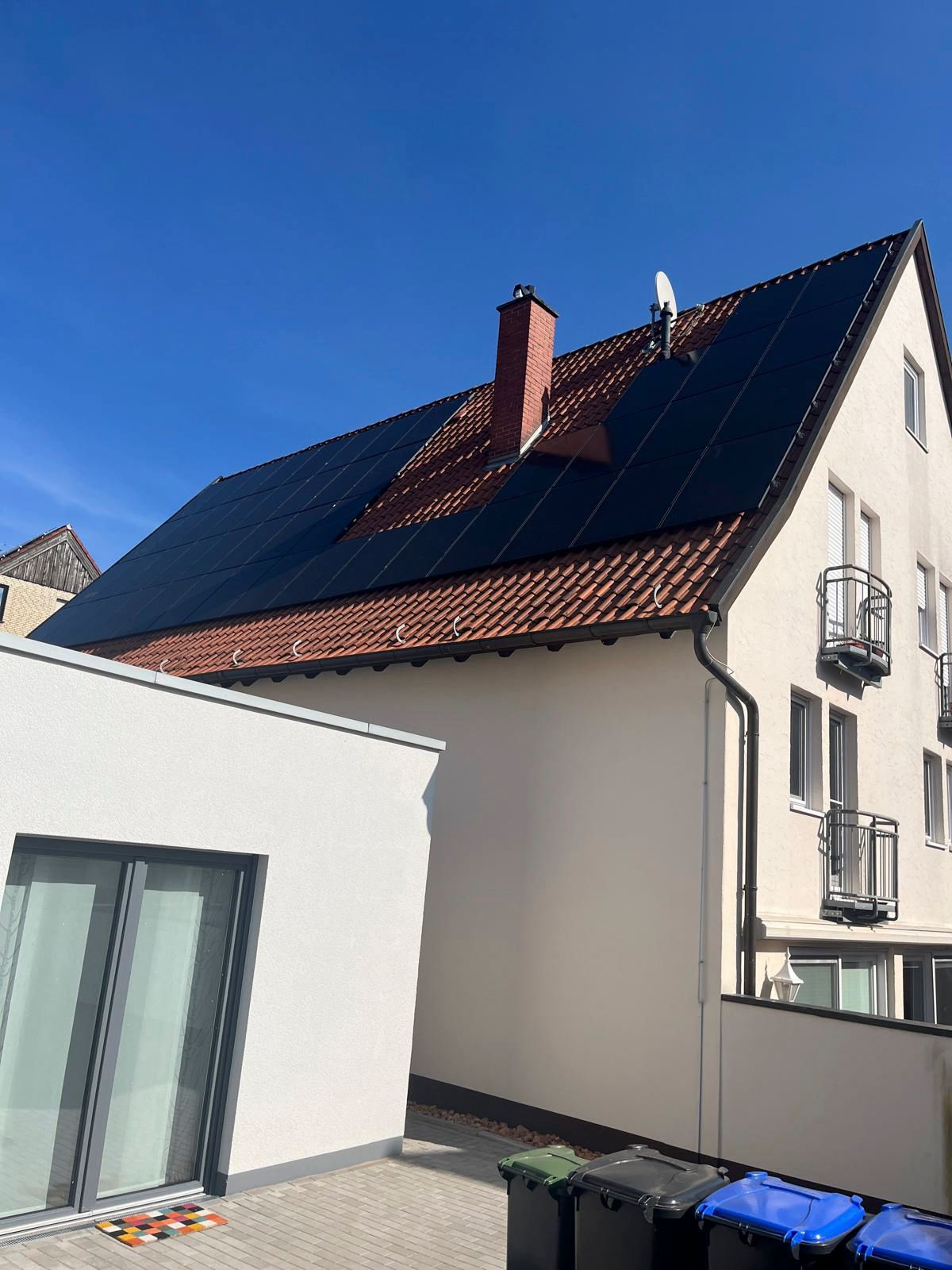 Solarpaneele auf dem roten Ziegeldach eines hellen Gebäudes unter klarem, blauem Himmel.