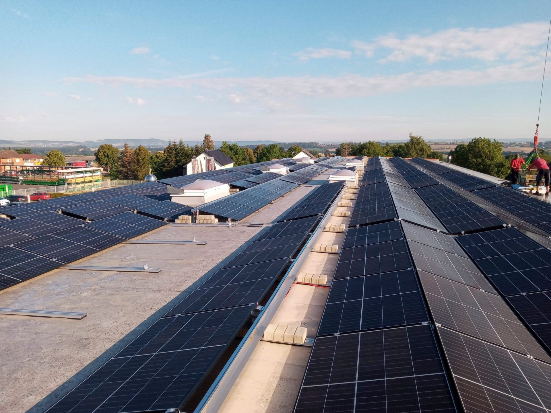Solarpaneele auf einem Gebäudedach, Arbeiter in der Ferne. Blauer Himmel darüber.