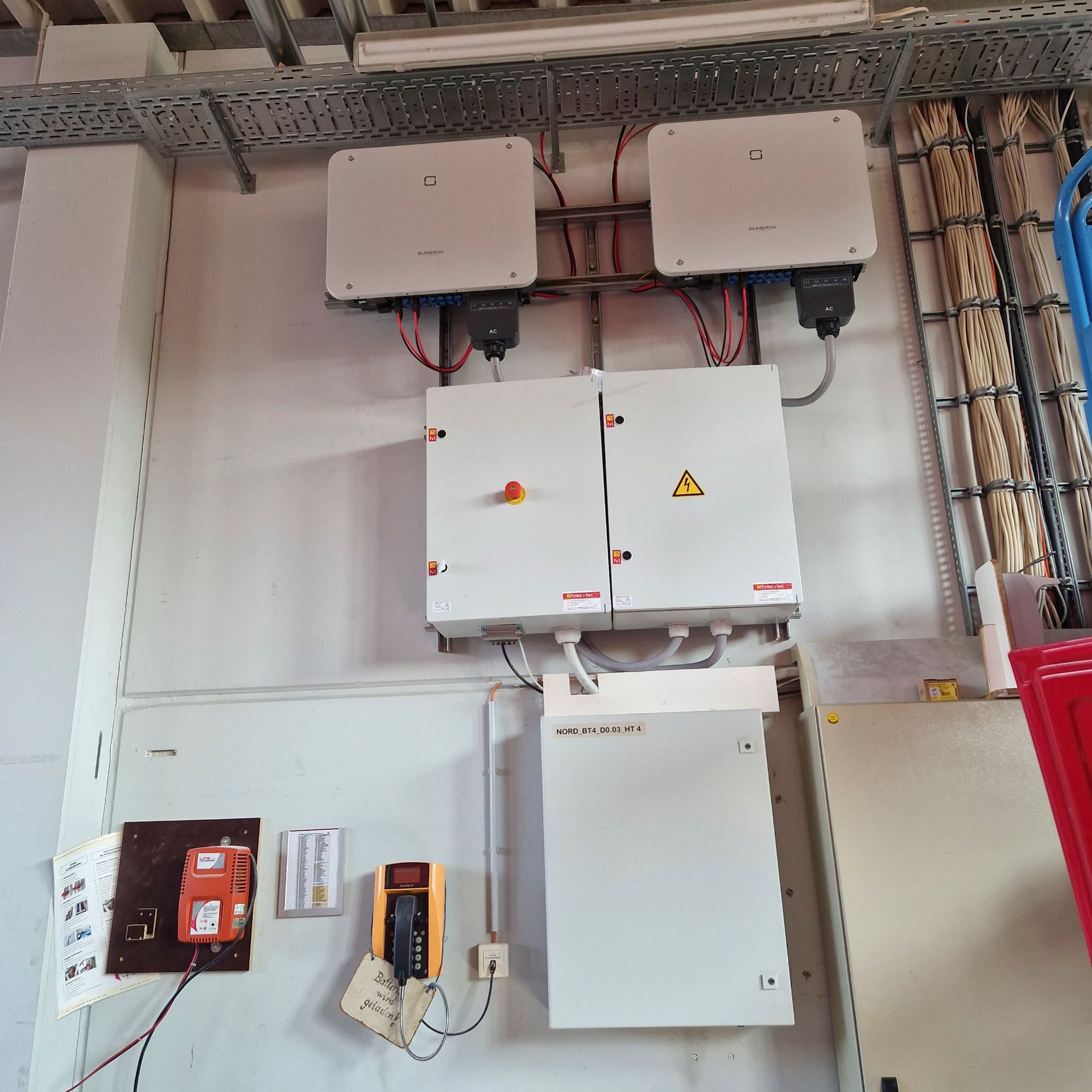 Elektrische Bauteile, die an einer Wand montiert sind: Wechselrichter, Sicherungsautomaten und Verkabelung.