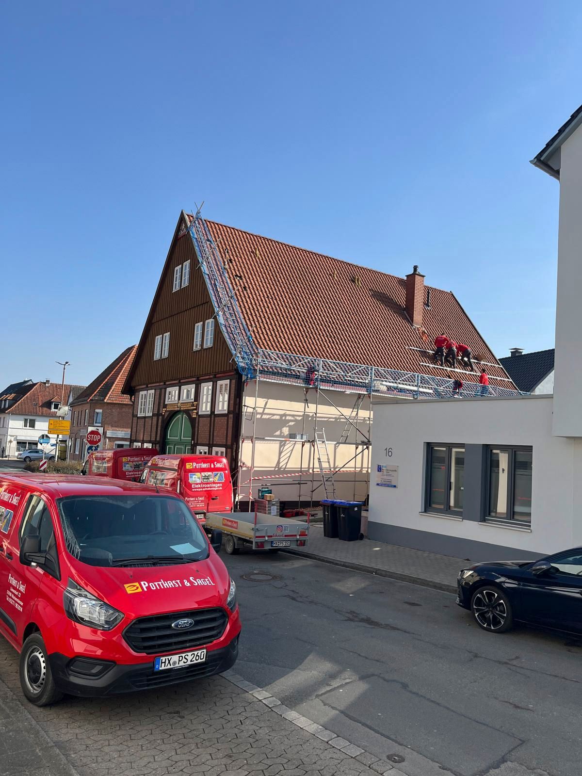 Arbeiter auf einem Dach, ein Gerüst um ein Gebäude, rote Lieferwagen auf der Straße. Strahlend blauer Himmel.