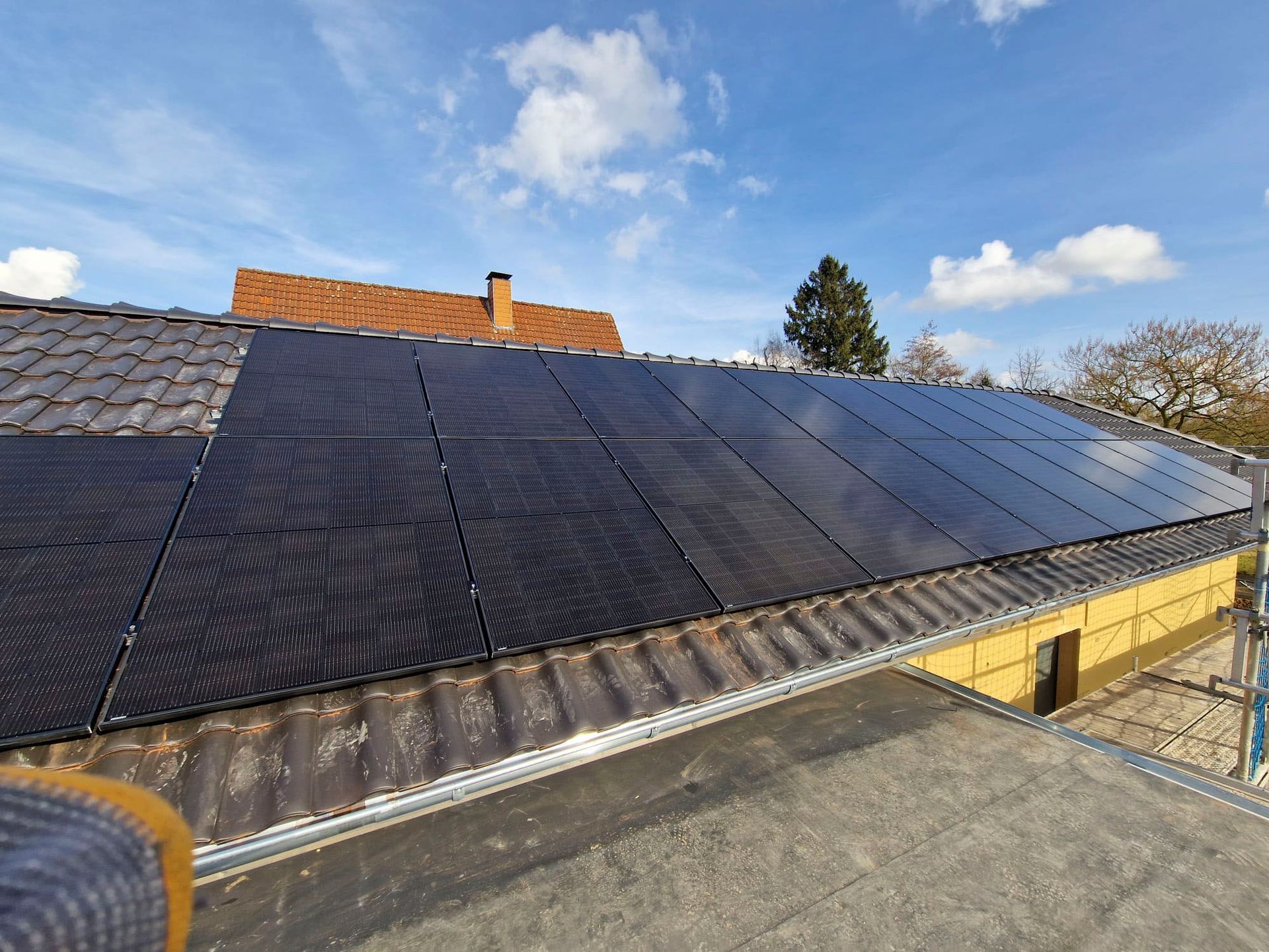 Auf einem Ziegeldach unter einem teilweise bewölkten Himmel wurden Solarpaneele installiert.