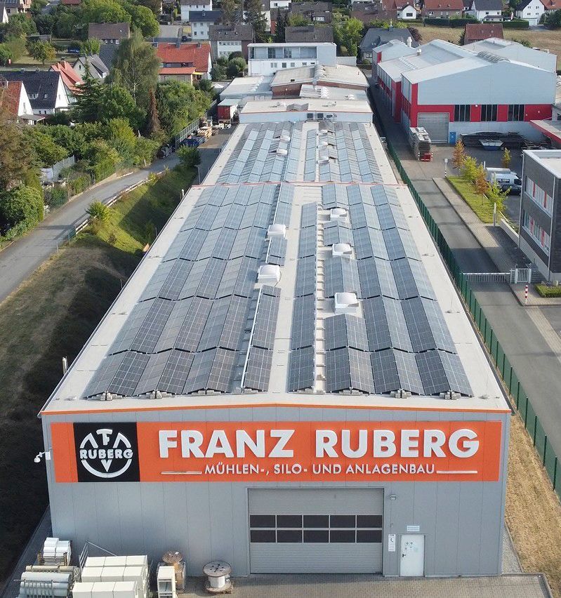 Gebäude mit Solarpaneelen, Franz-Ruberg-Schild, weiß, orange und grau, deutscher Text.