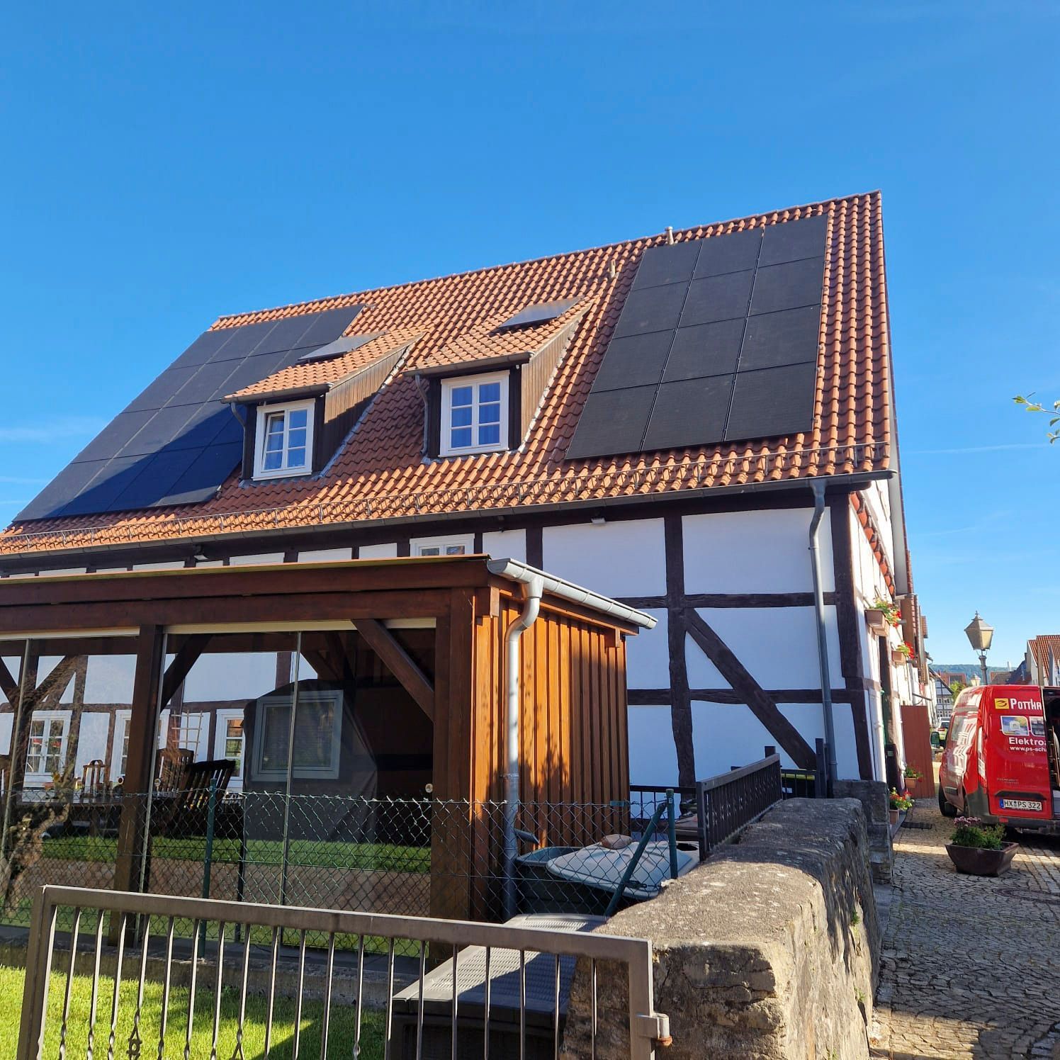 Fachwerkhaus mit rotem Ziegeldach und Solaranlage. Dachüberstand mit Holzbalken und kleinen Fenstern.