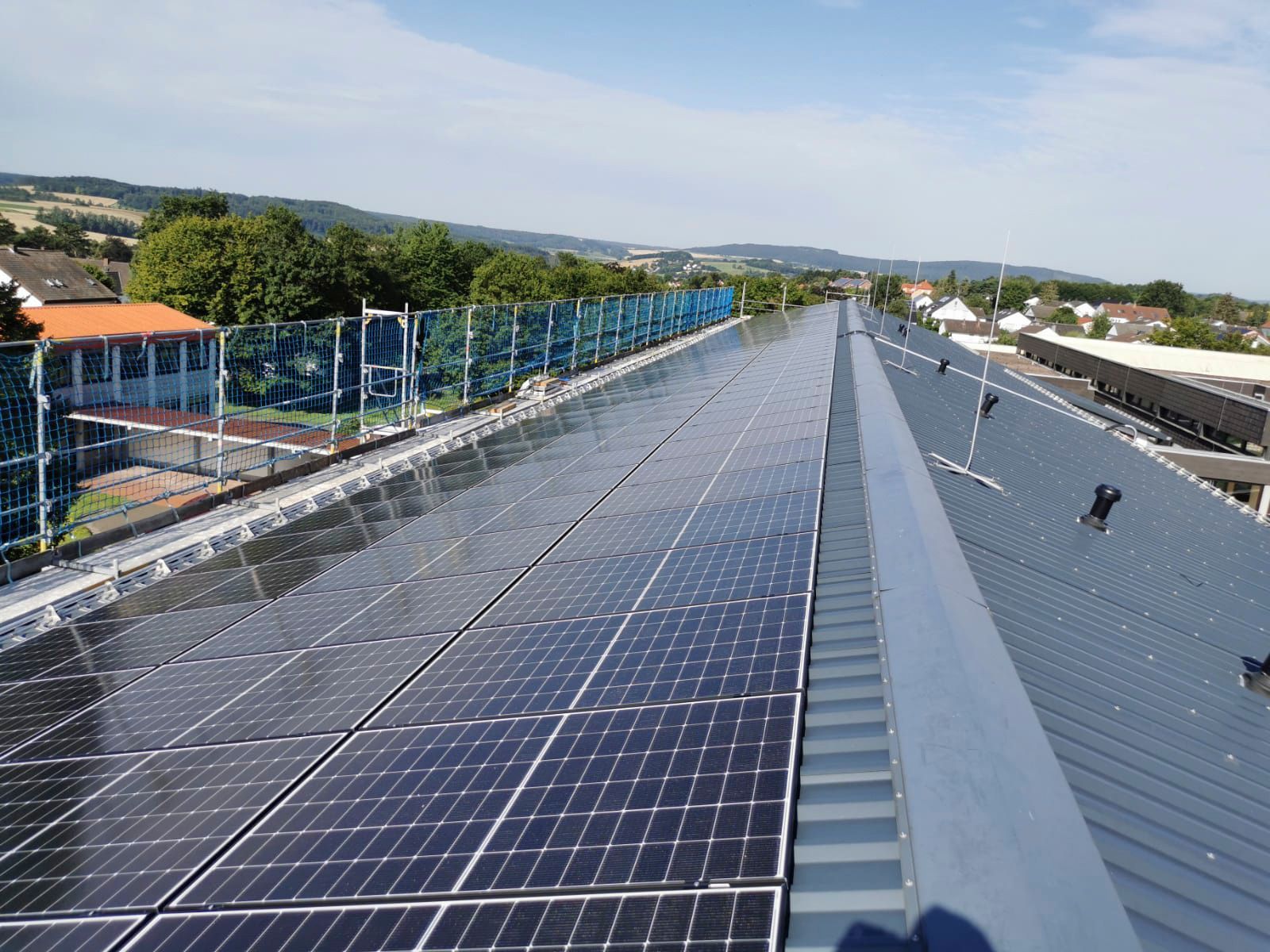 Solarpaneele auf einem Metalldach, im Hintergrund blauer Himmel und Stadtkulisse in der Ferne.