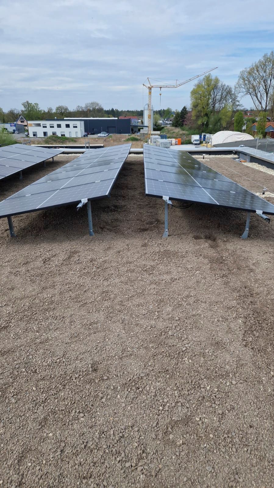 Solarpaneele im Freien installiert, Kiesboden. Baukran im Hintergrund. Bewölkter Himmel.