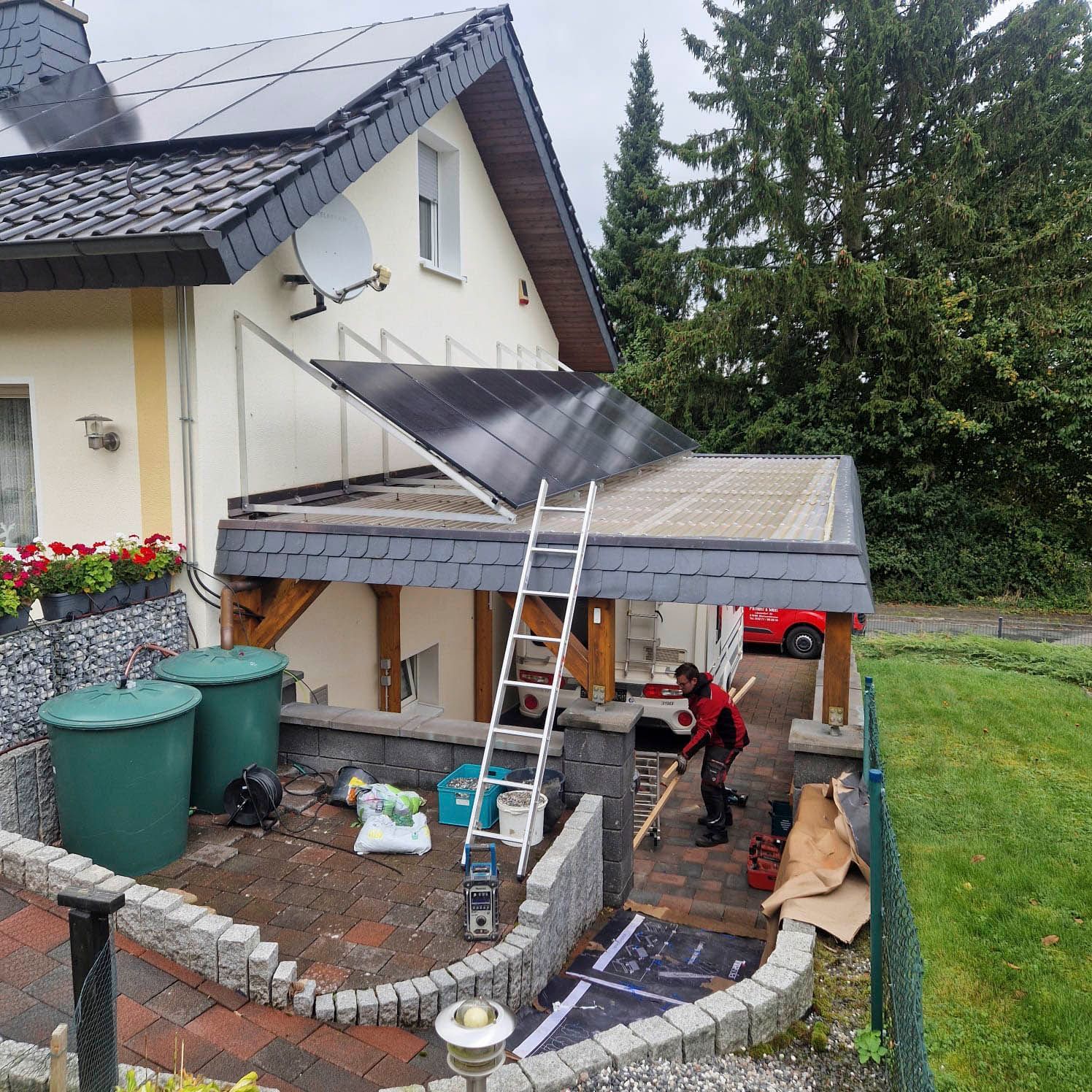 Installation von Solarmodulen auf einem Haus mit Carport. Ein Arbeiter befindet sich auf dem Dach.