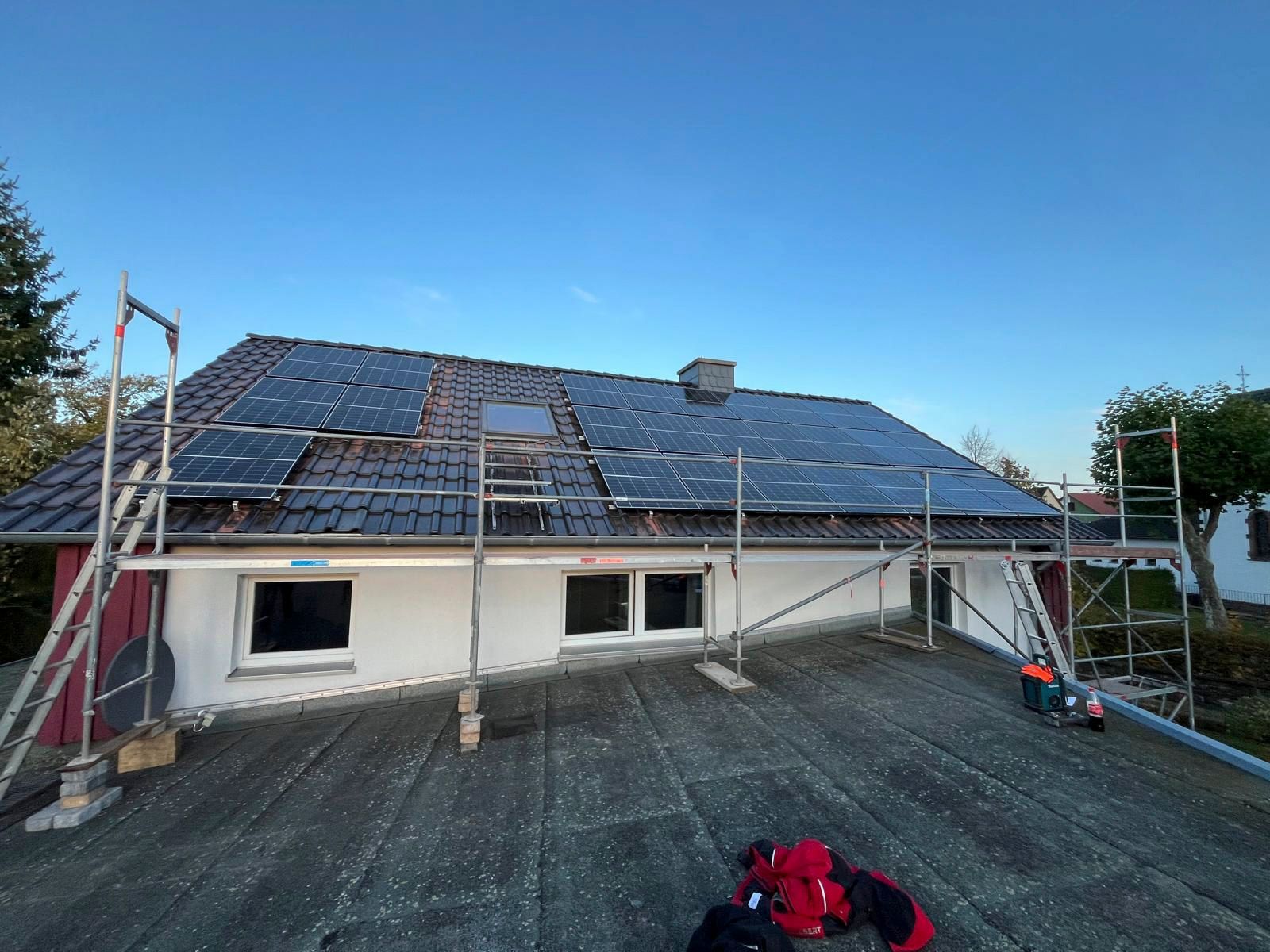 Auf einem Wohnhausdach wurden mit Gerüsten Solarpaneele installiert. Blauer Himmel darüber.