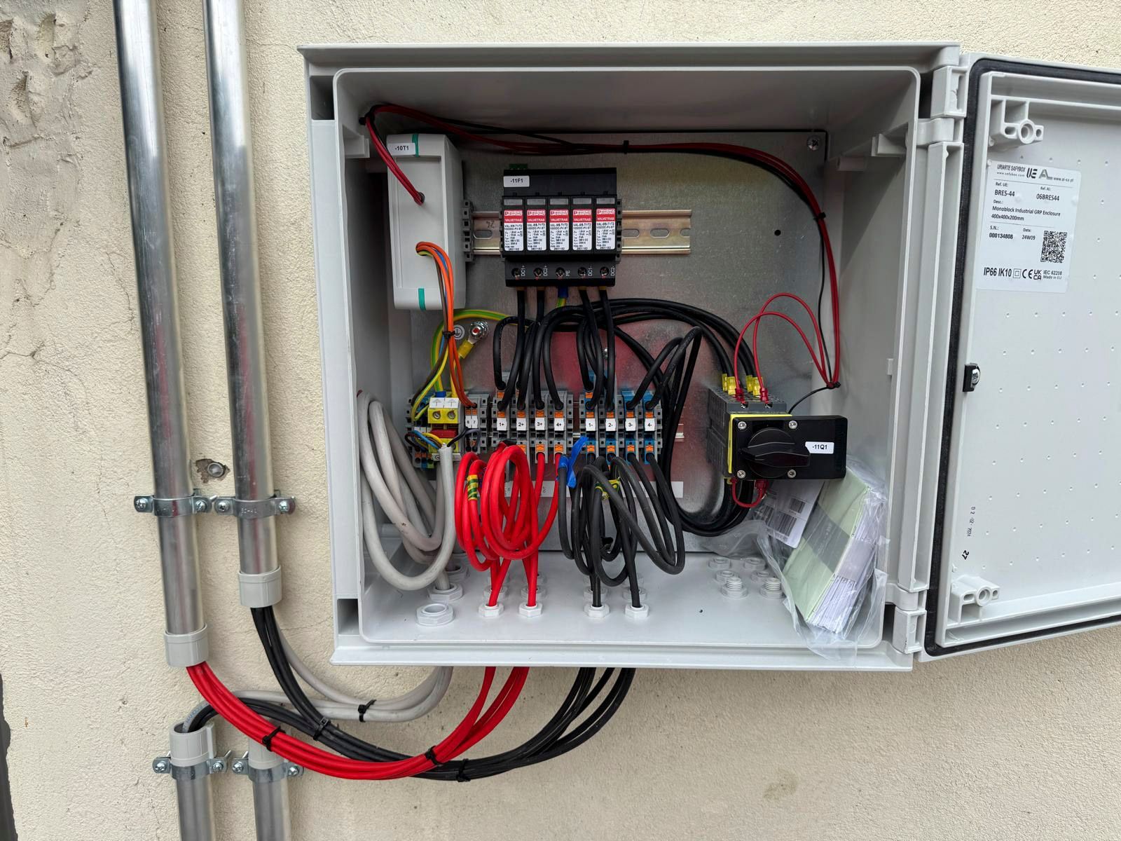 Offener Elektroverteilerkasten an der Wand, Sicherungen und Leitungen. Rote, schwarze und weiße Drähte sind sichtbar.