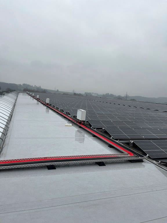 Solaranlage auf dem Dach mit roten Sicherheitsabsperrungen; bedeckter Himmel.