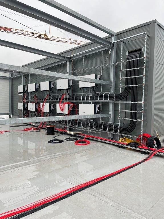 Installation elektrischer Anlagen: mehrere weiße Wechselrichter auf Metallgestellen, rote und schwarze Kabel