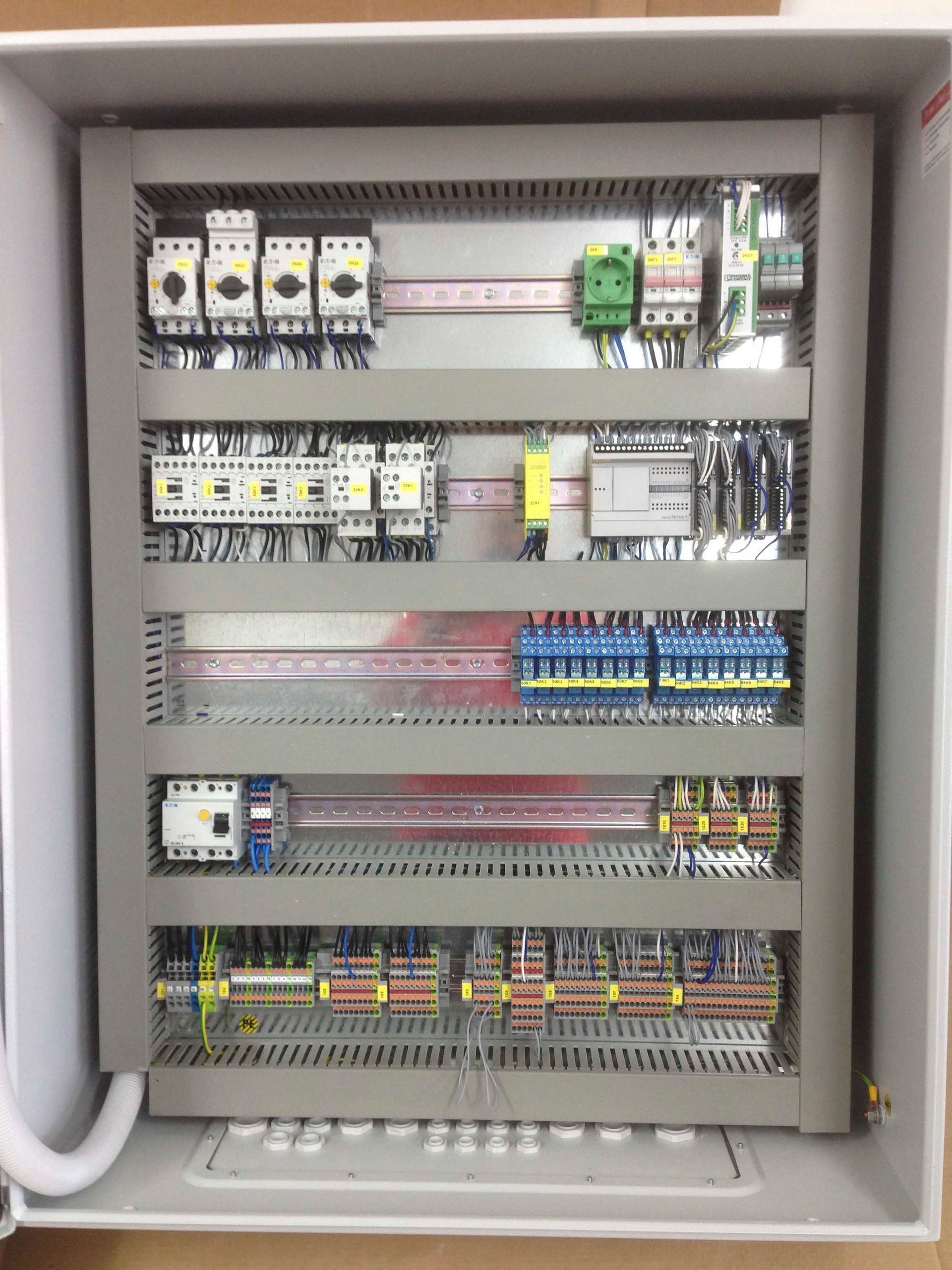 Elektrischer Schaltschrank mit verschiedenen Bauteilen, Drähten und Anschlüssen in einem Metallgehäuse.