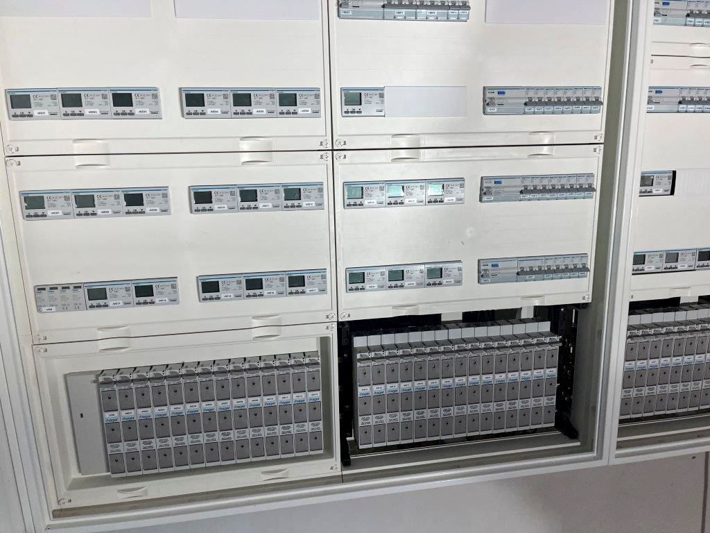 Weißer elektrischer Schaltschrank mit Reihen von Messgeräten und Leistungsschaltern.
