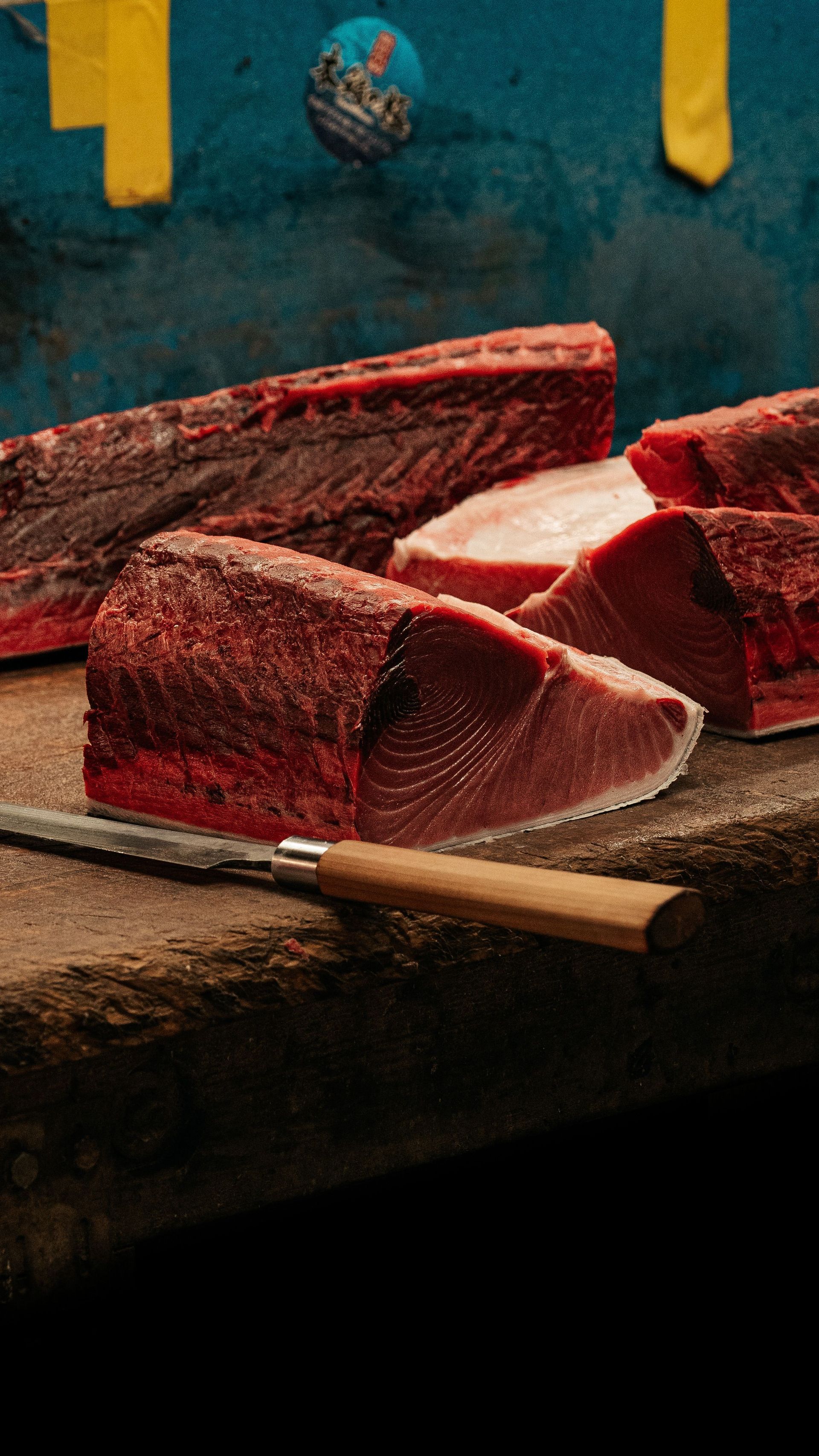 Filetes rojos crudos sobre una tabla de cortar con un cuchillo, sobre un fondo oscuro y tiras amarillas colgantes.