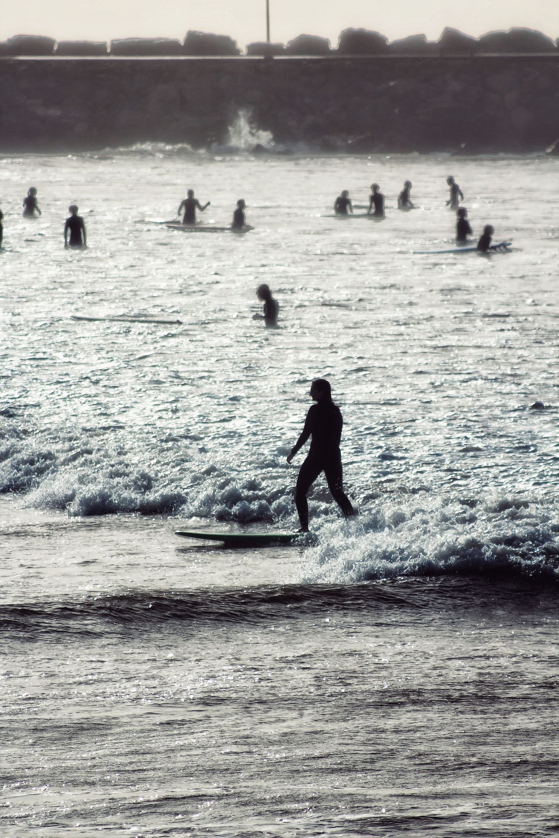 Un surfista cabalga una pequeña ola mientras unos nadadores flotan al fondo cerca de la orilla.