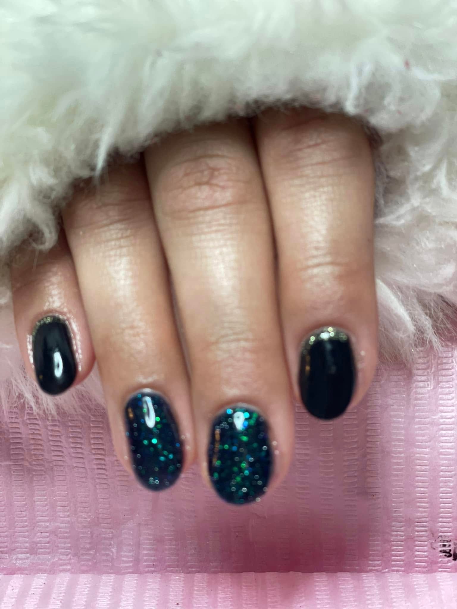 Mano con uñas pintadas en tonos azul oscuro, con acentos de brillo y punta dorada.