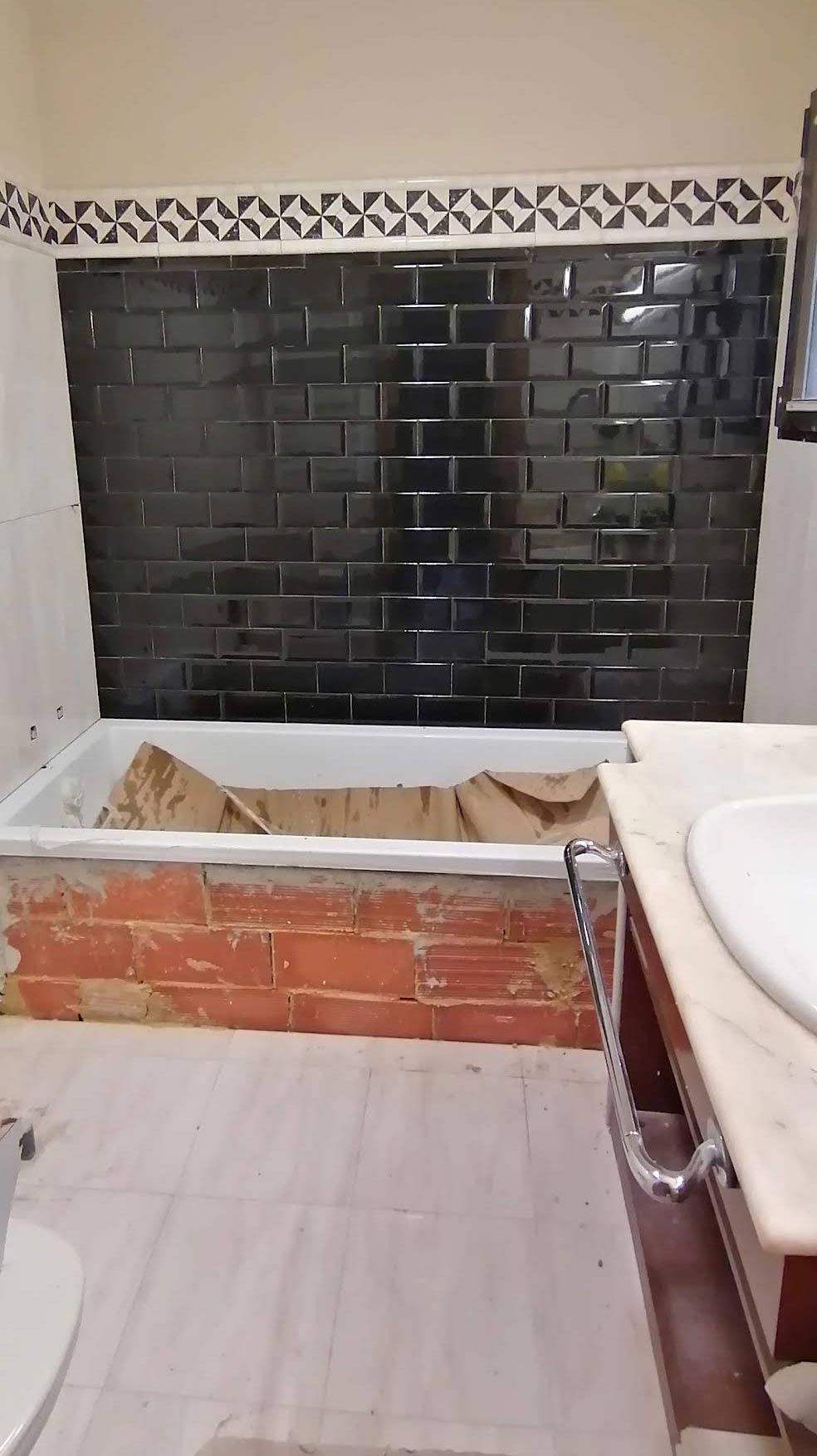 Una renovación de baño en progreso, que presenta una pared de ladrillo negro recién revestida sobre una bañera con un delantal de ladrillo a la vista.
