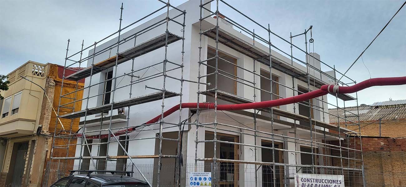 Edificio en remodelación con andamios. Tubo rojo que se extiende transversalmente. Paredes amarillas y blancas. Día nublado.
