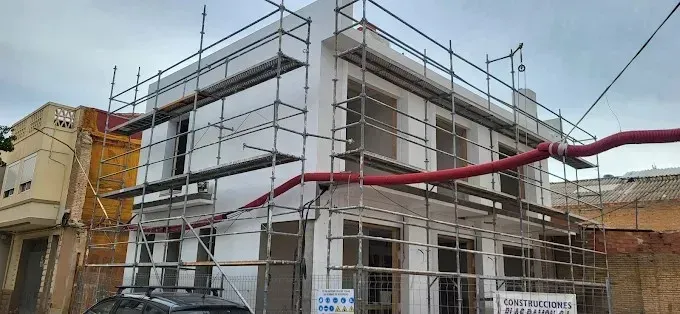 Edificio en remodelación con andamios. Tubo rojo que se extiende transversalmente. Paredes amarillas y blancas. Día nublado.