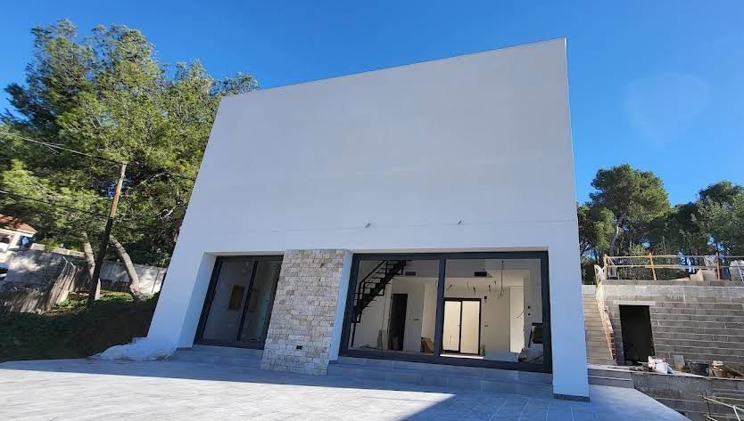 Mano enguantada, cortando cables eléctricos con alicates en un enchufe. Bobina de cable gris al fondo.