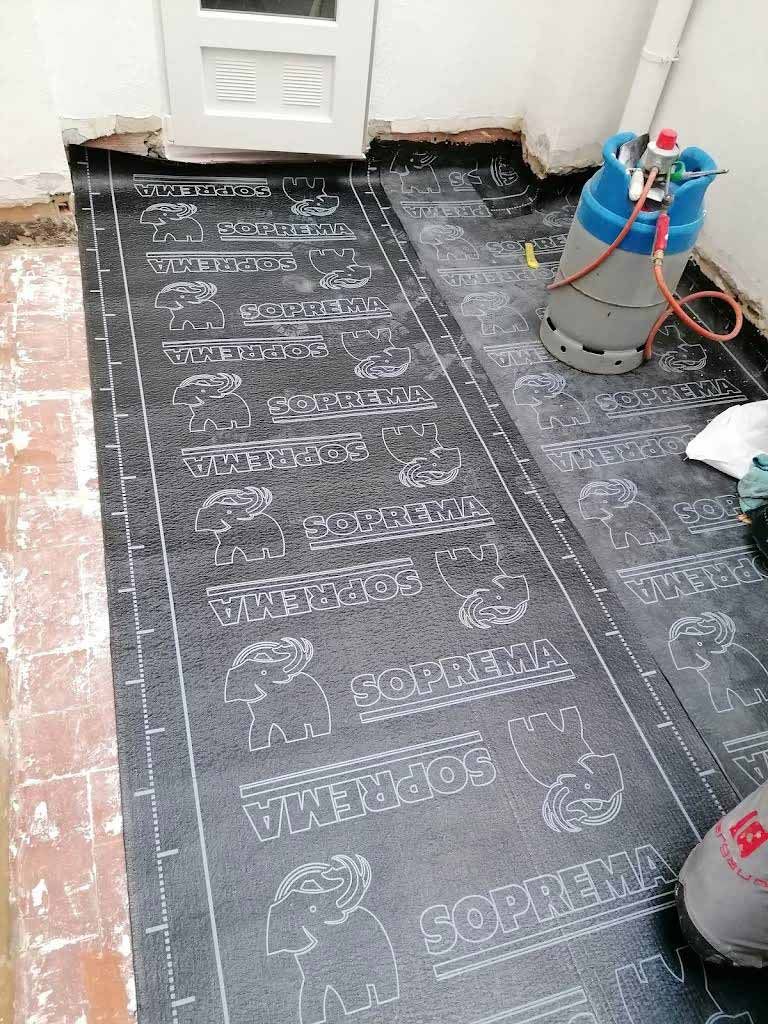 Se colocan rollos de membrana impermeabilizante de betún negro sobre el suelo, con una bombona de gas para aplicarla con soplete cerca.