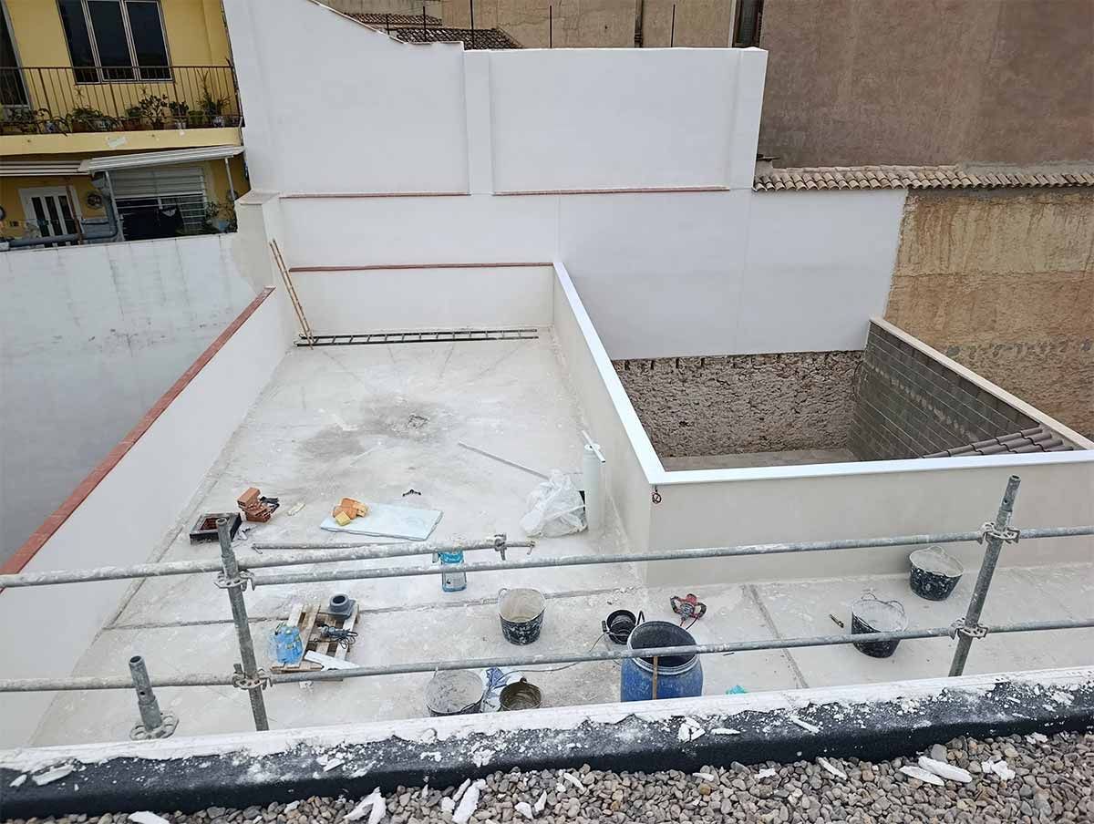 Sitio de construcción en la azotea de un edificio que muestra paredes blancas, un área hundida sin terminar y varias herramientas en el piso.