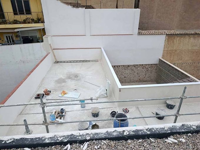 Sitio de construcción en la azotea de un edificio que muestra paredes blancas, un área hundida sin terminar y varias herramientas en el piso.