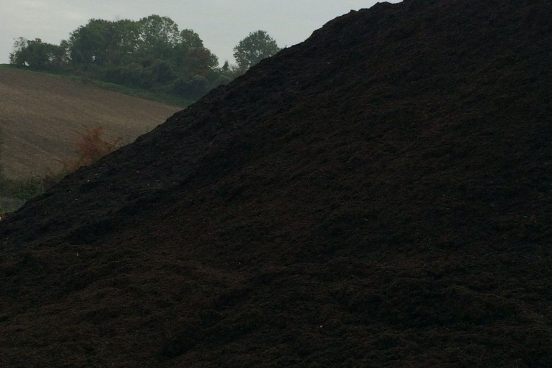 Gros tas de compost brun foncé en extérieur, avec un paysage rural en arrière-plan.