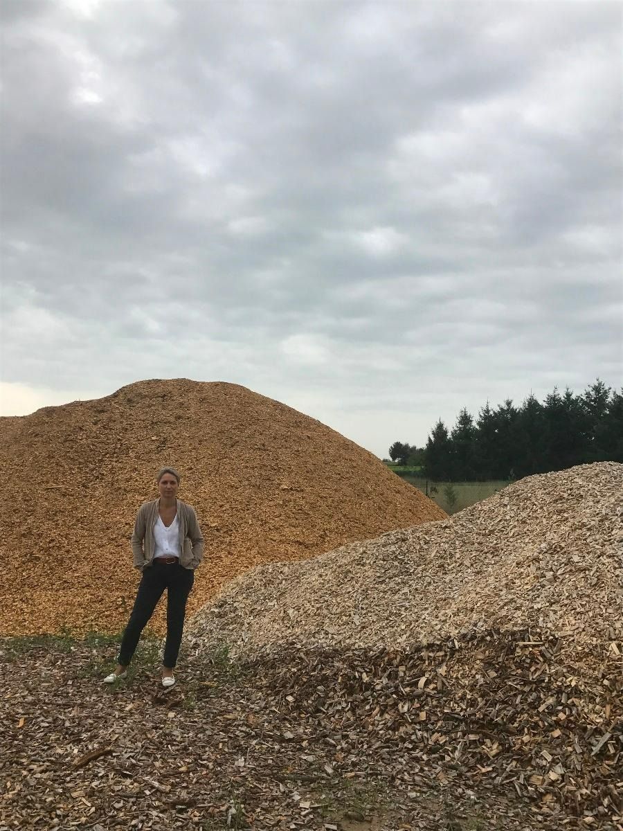 Une femme se tient près de grands tas de copeaux de bois sous un ciel nuageux.
