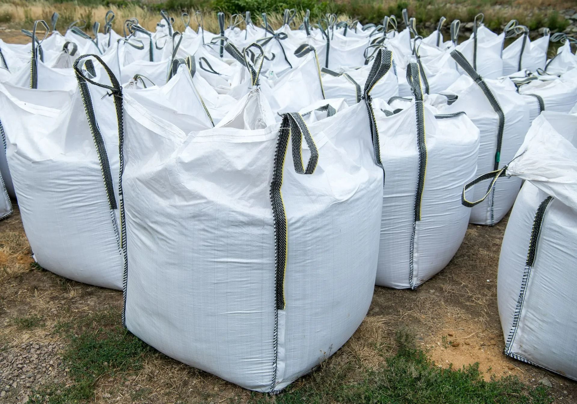 Des sacs blancs en vrac avec des sangles noires posés au sol, contenant probablement des matériaux de transport.