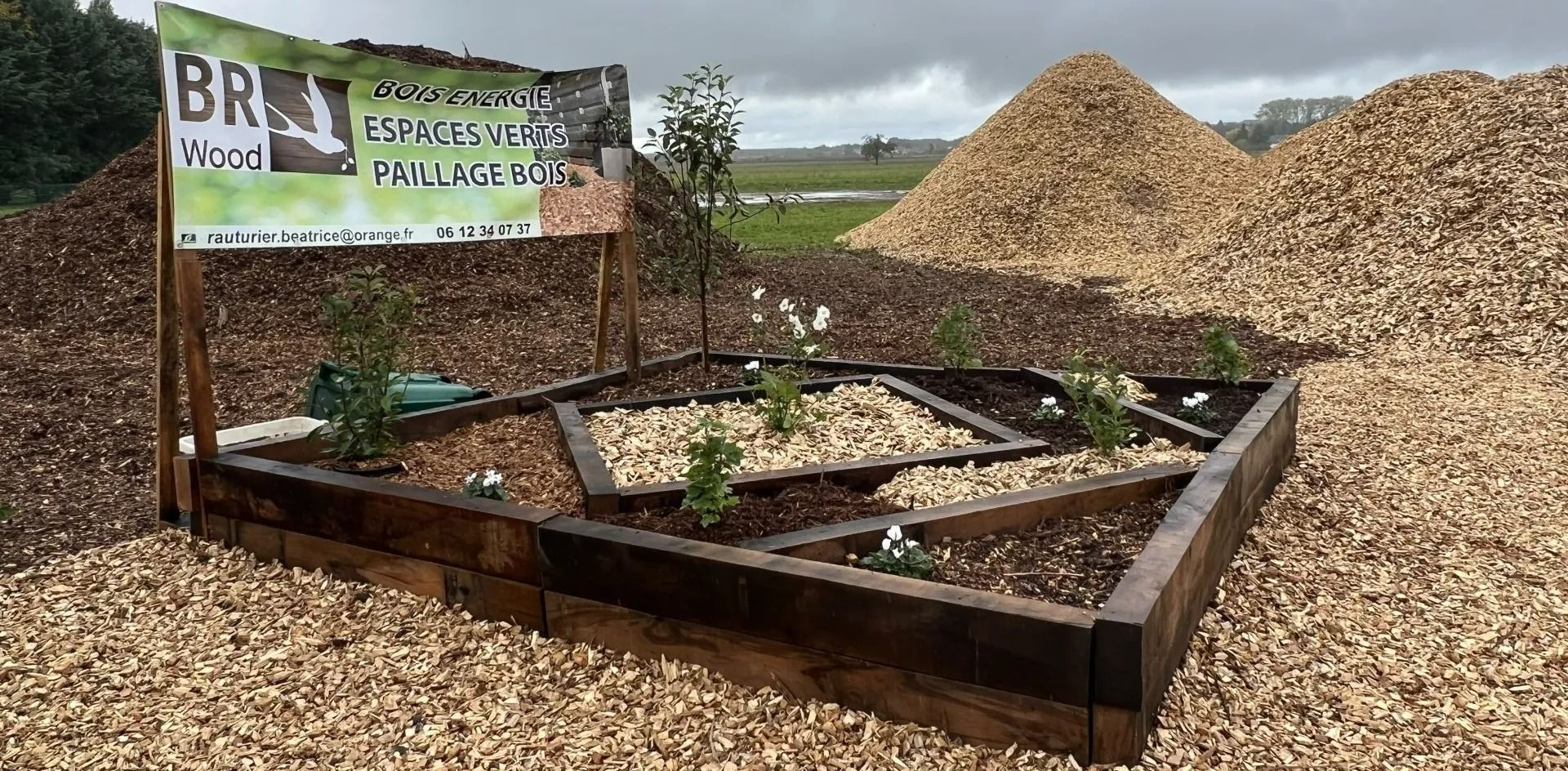 Un parterre surélevé avec des plantes, des copeaux de bois et de grands tas de copeaux de bois en arrière-plan.