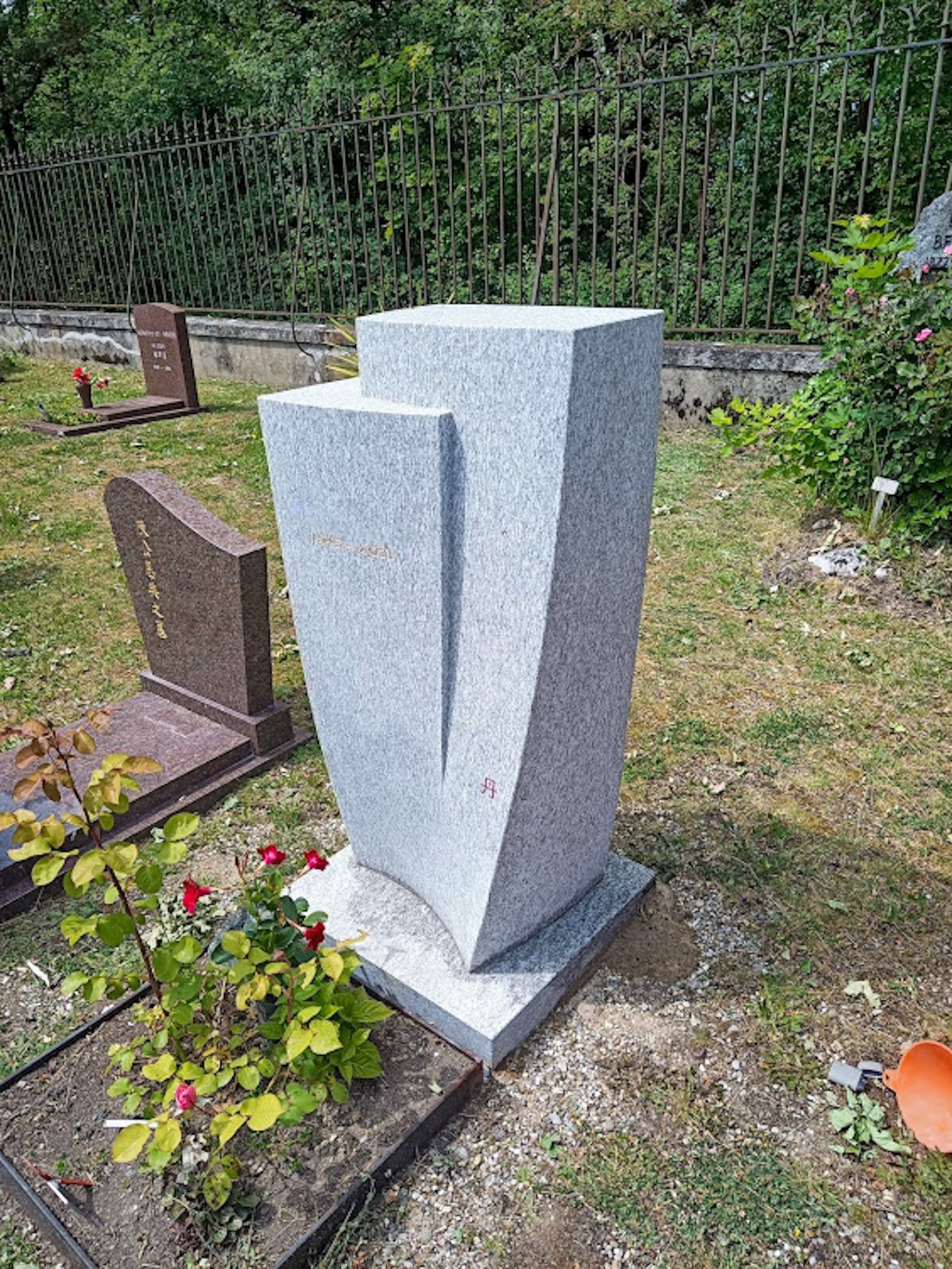 Ein Grabstein auf einem Friedhof mit einem Zaun im Hintergrund.