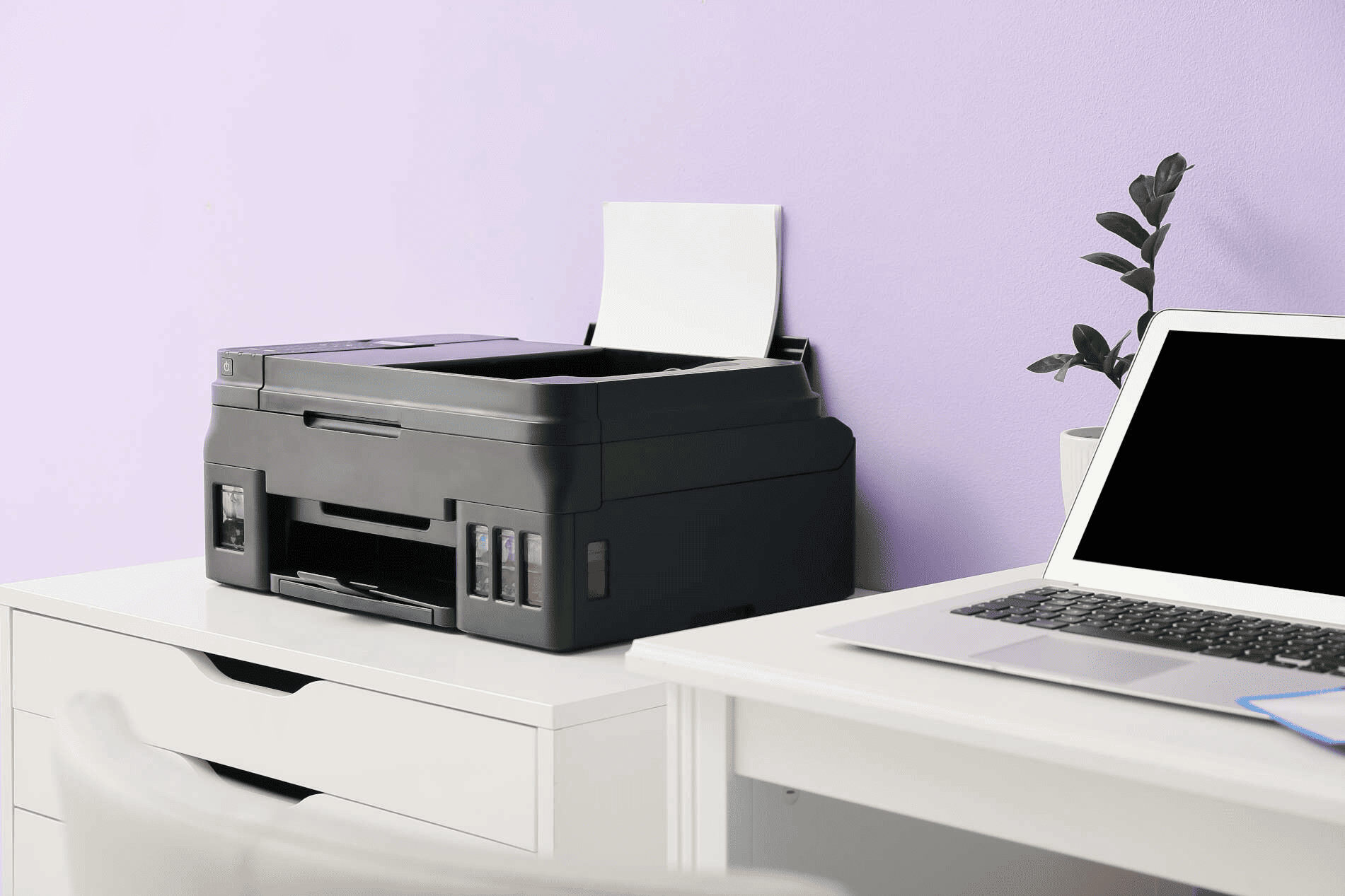 Hay una impresora en un escritorio al lado de una computadora portátil.