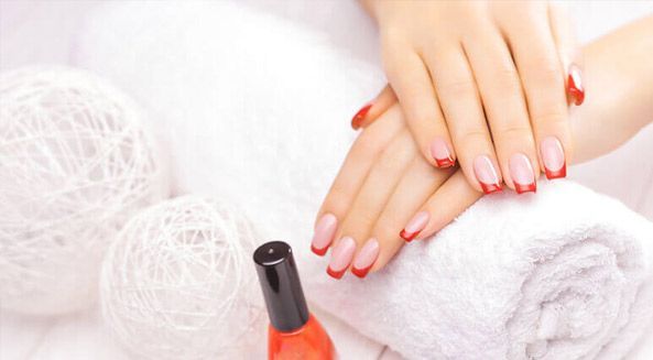 Las manos de una mujer con manicura francesa roja sobre una toalla junto a una botella de esmalte de uñas.